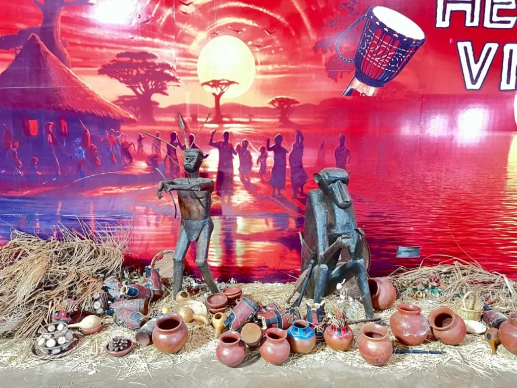 Carved figures and clay pots before the sunset mural